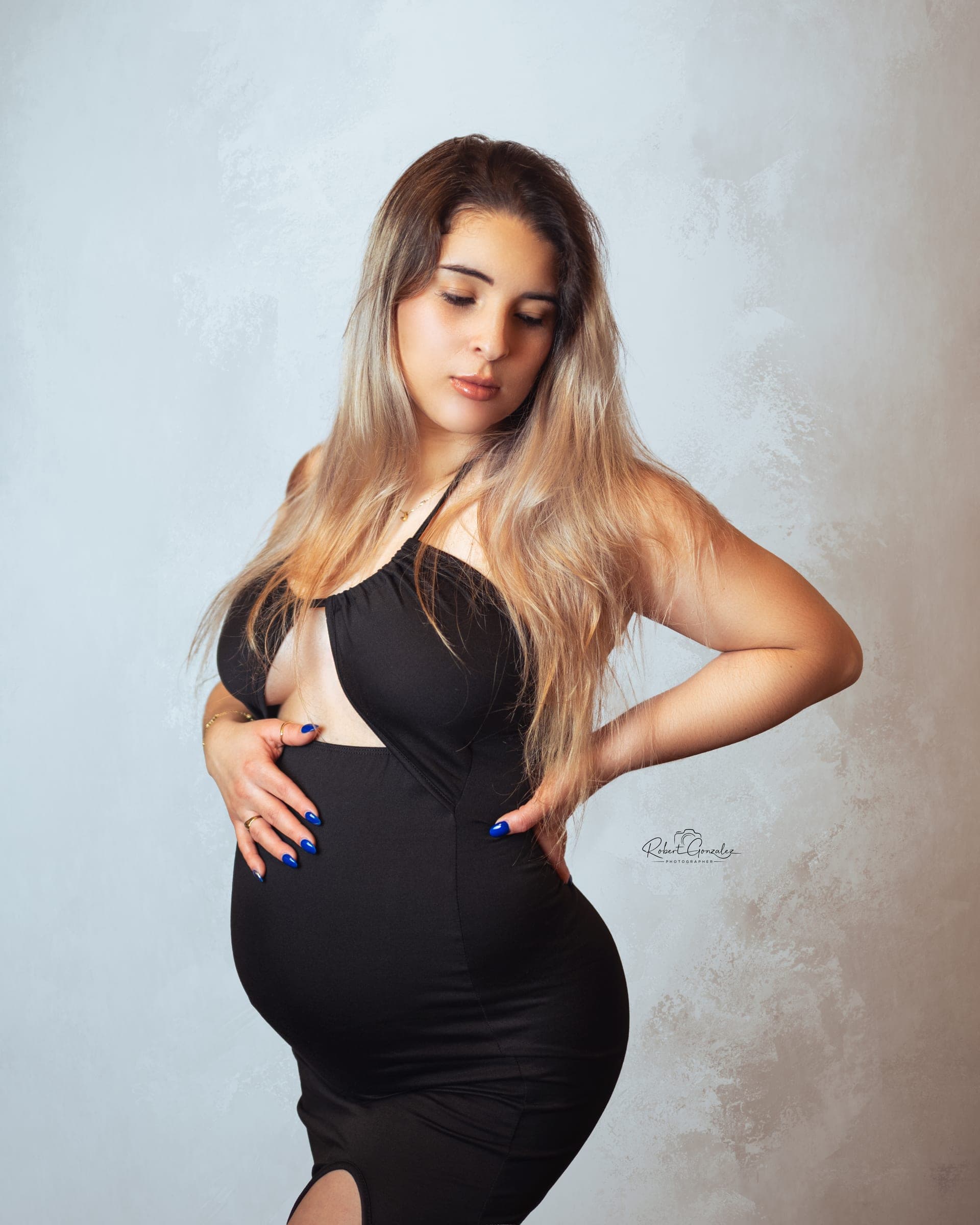 Maternity session: mother-to-be in a black dress against a light backdrop