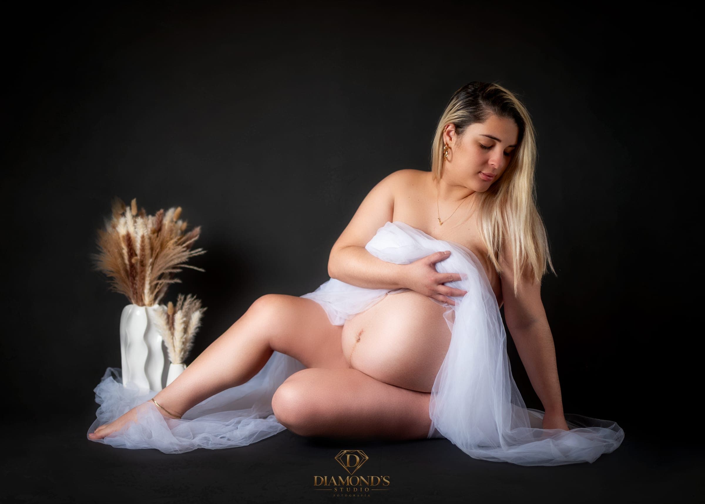 Maternity session: seated in white tulle beside dried flowers, black backdrop