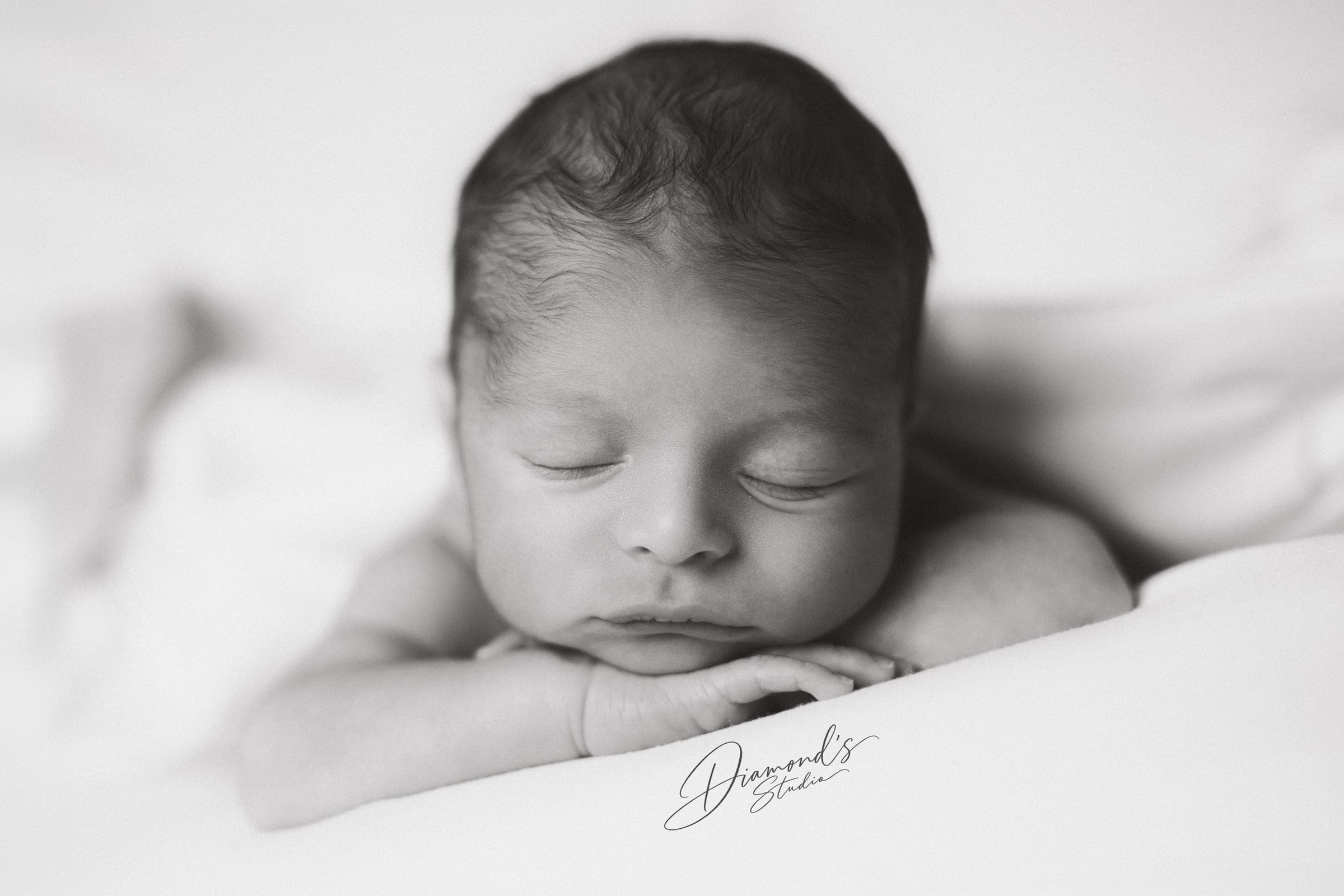 Sesión newborn: recién nacido dormido sobre sus manitas, en blanco y negro